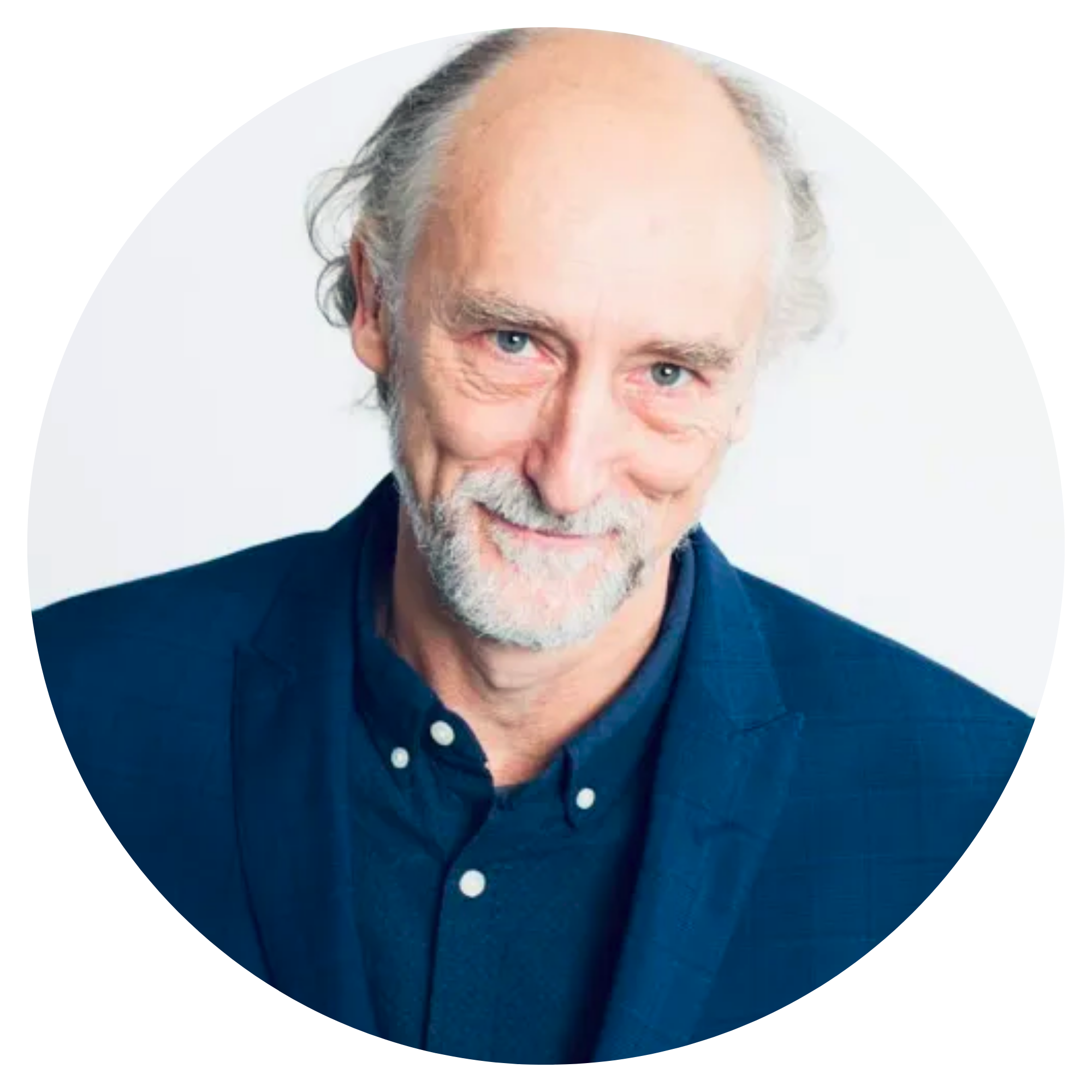 Man with grey hair wearing dark blue shirt and blazer.