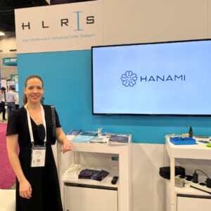 A woman stands at the HANAMI booth during an HPC event, next to a display screen showing the HANAMI logo.
