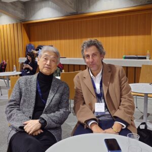 Two man sitting on wooden chairs and posing for the photo.