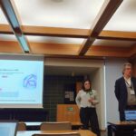 A man presenting a talk about the HANAMI project standing in front of a screen and a woman behind him.
