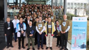 Group photo of participants and organisers at the ACM Asian School on HPC and AI, standing outside the venue beside an event banner, wearing conference badges and event t-shirts.