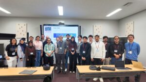 Group photo of participants and organisers at the ACM Asian School, standing in a classroom in front of a screen displaying the event webpage.