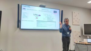 Speaker presenting during a tutorial session, holding a microphone in front of a screen displaying useful links and resources for the Yambo code.